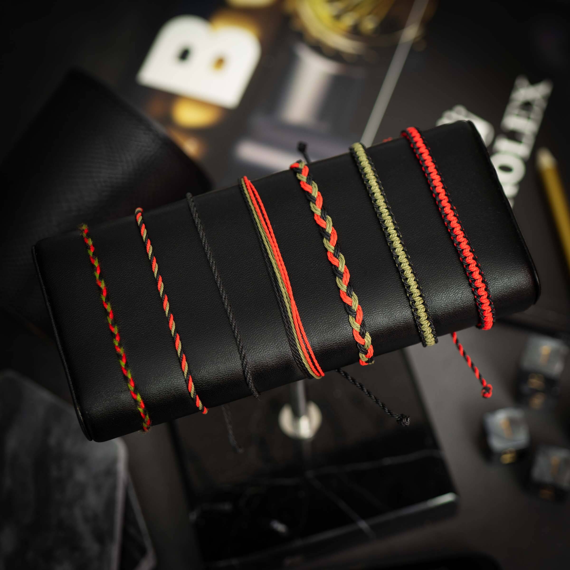 A collection of seven vintage-style bracelets with a black and red color scheme, displayed on a stand against a backdrop featuring a watch and other accessories.