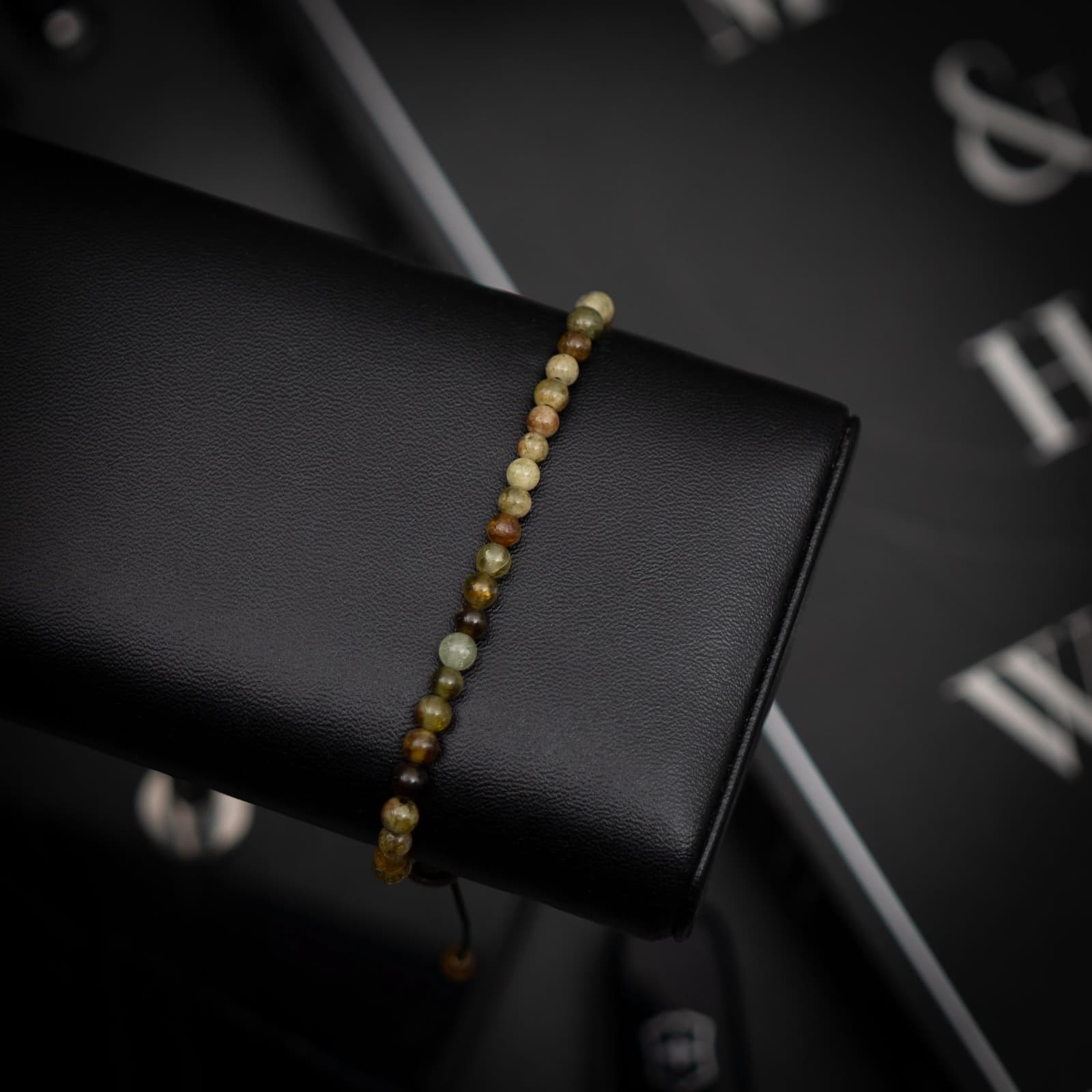 A green garnet gemstone bracelet displayed on a black stand with a blurred background.