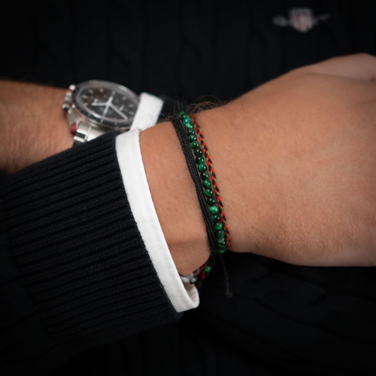 An image showing three bracelets on a person's wrist. The bracelets are made of green and black materials, including green tiger's eye gemstones.