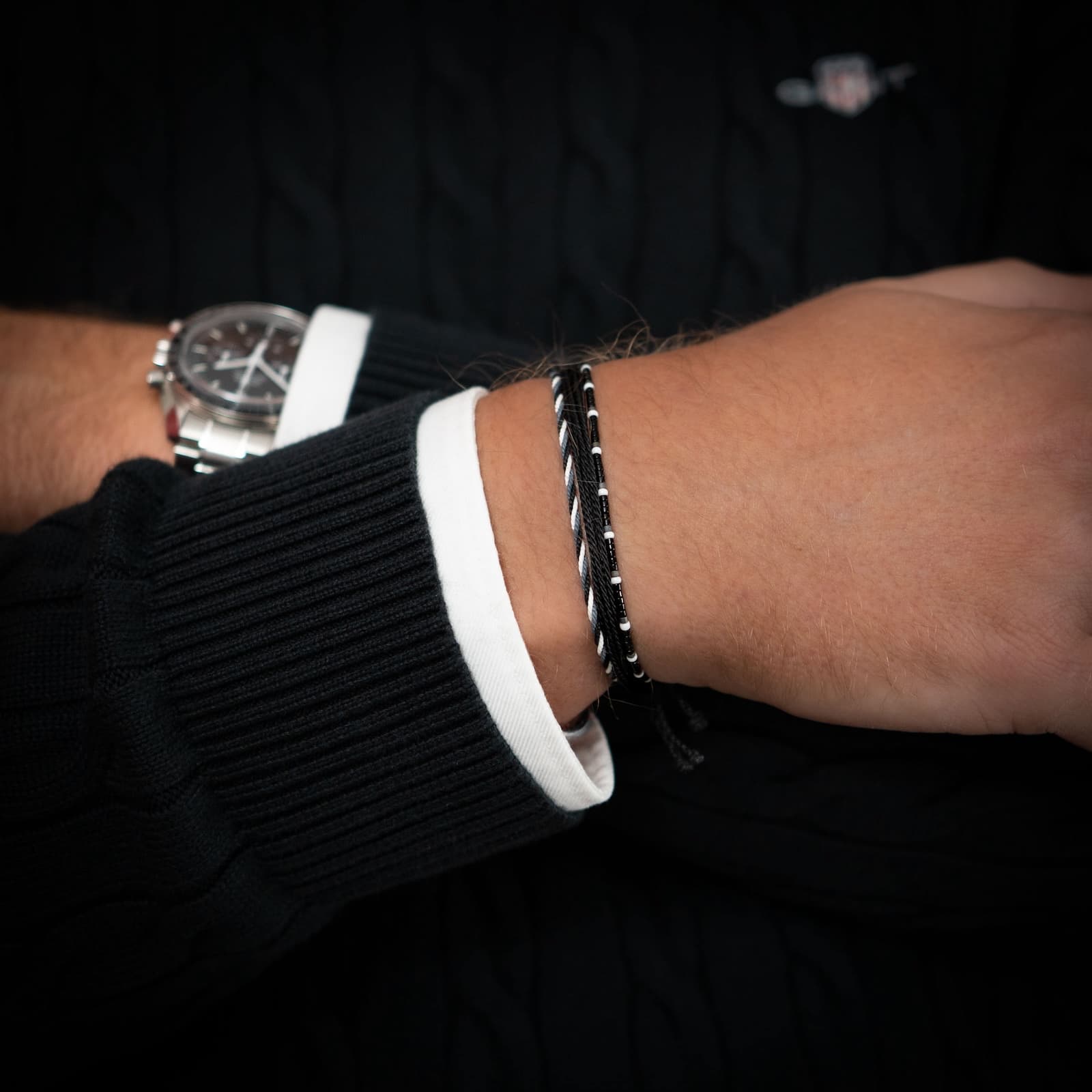 An image showing a wrist wearing two bracelets, one black and one white, with a gunmetal charm, on a textured background.