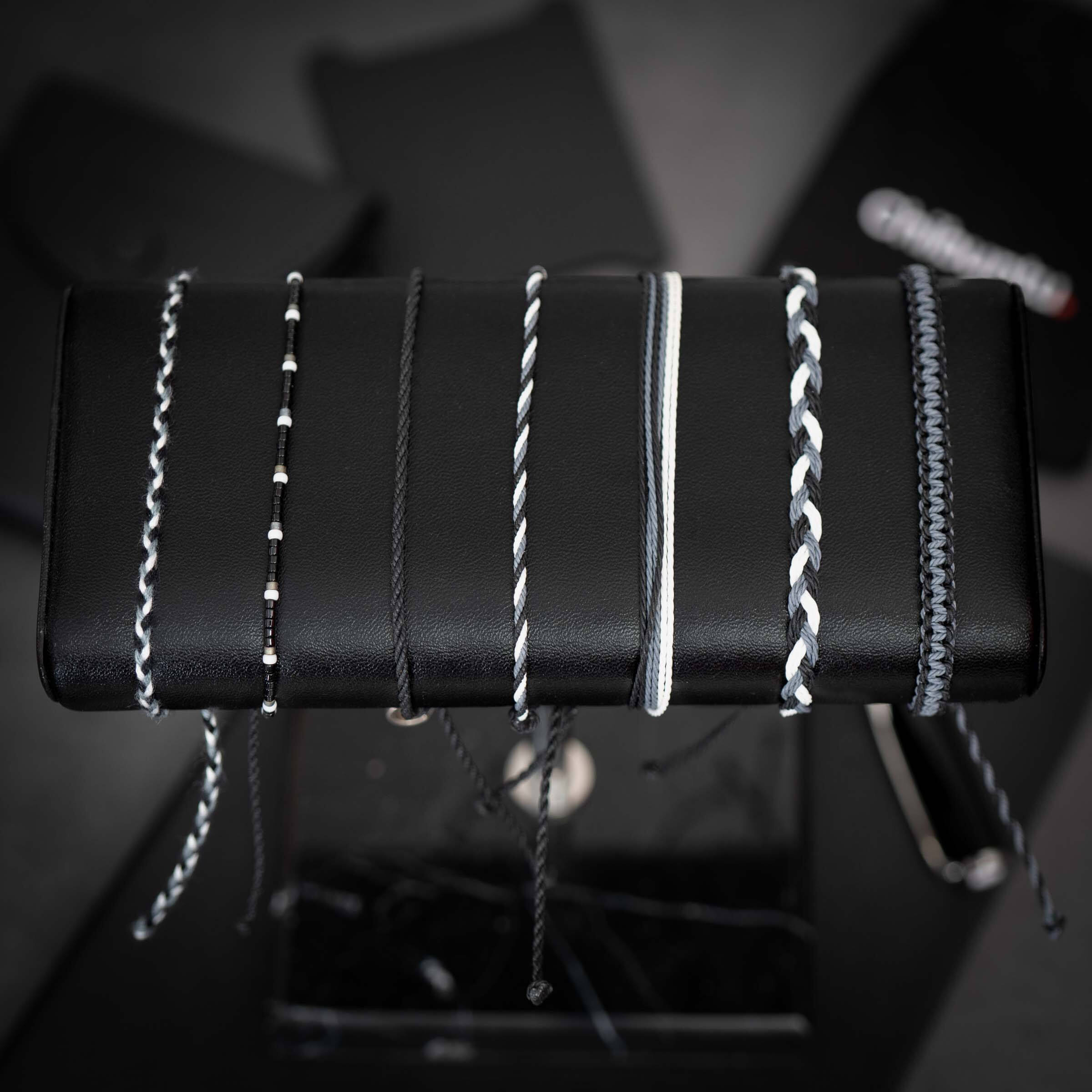 A collection of James Bond-themed bracelets displayed on a stand, featuring various designs including beaded and strap styles, with a Chibuntu charm.