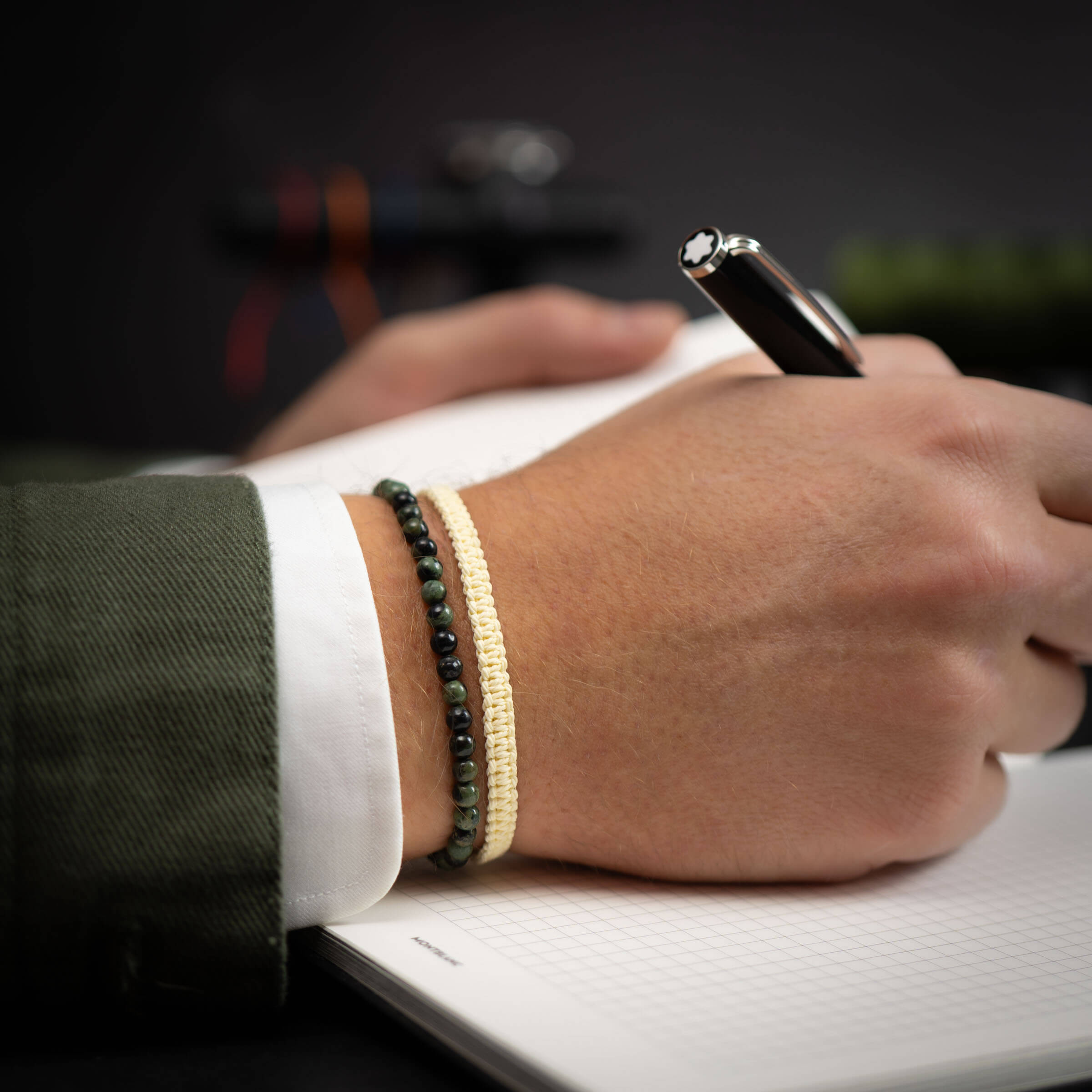 A person's wrist wearing a Moss Agate and Off-white bracelet while writing in a notebook.