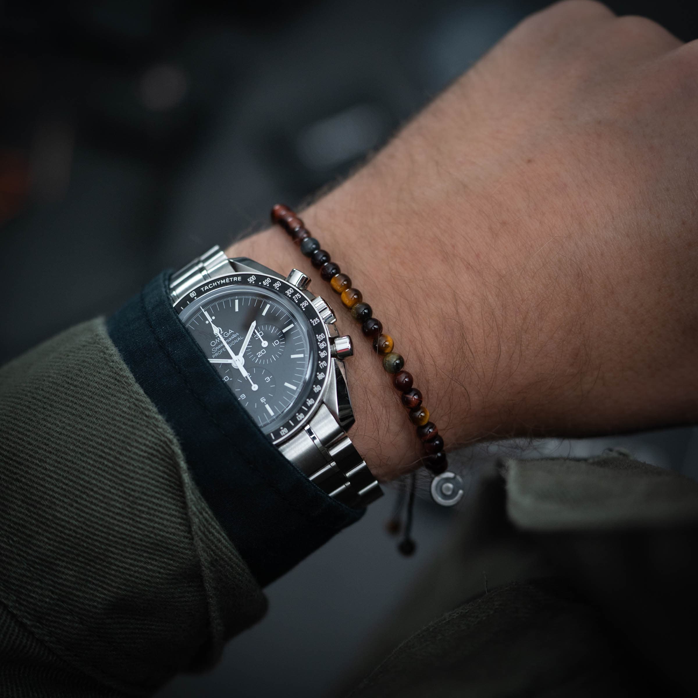 multi color tiger's eye bracelet with meaning next to an Omega Speedmaster