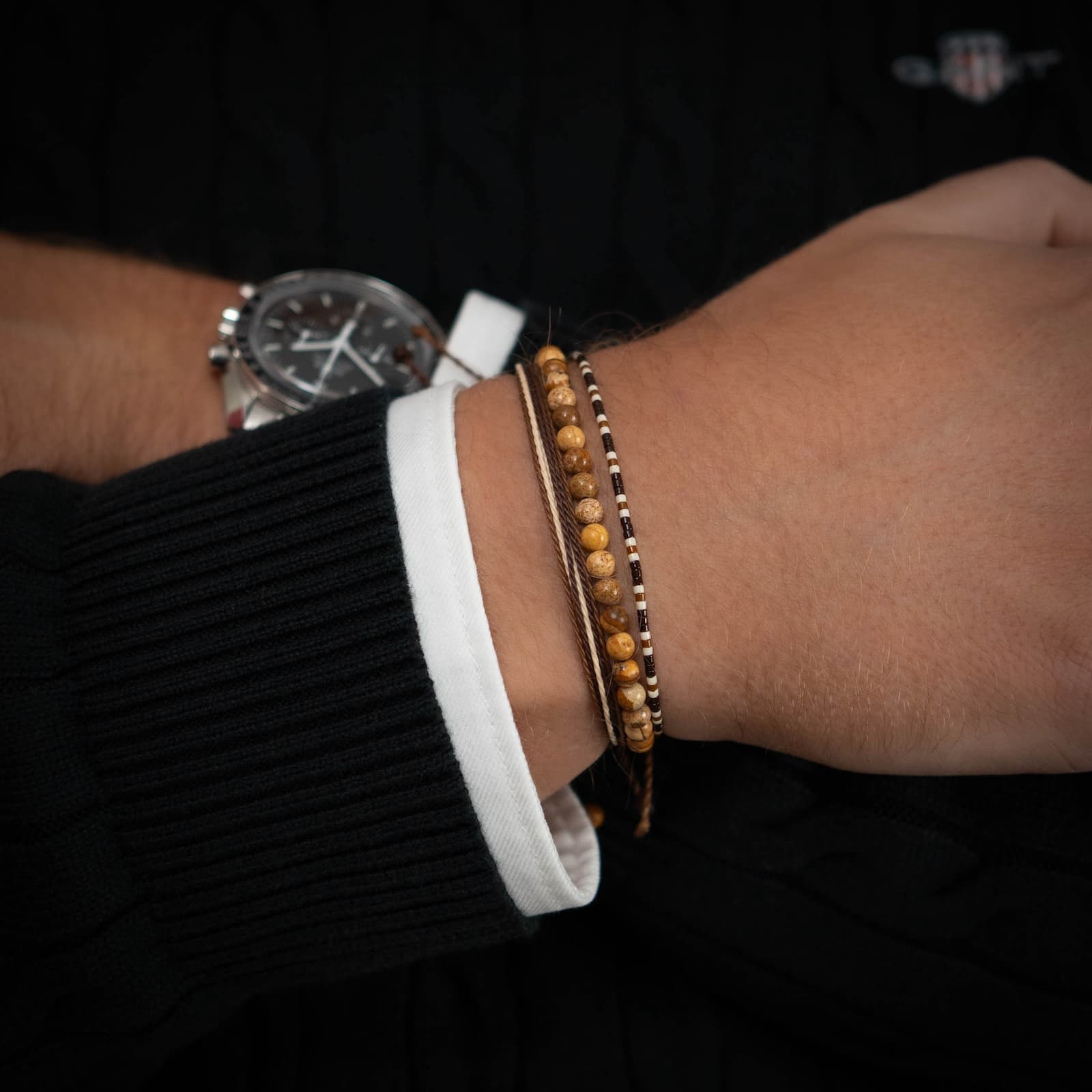 An image showing three gemstone bracelets on a person's wrist, with one featuring a watch, indicating the bracelets are worn alongside other accessories.