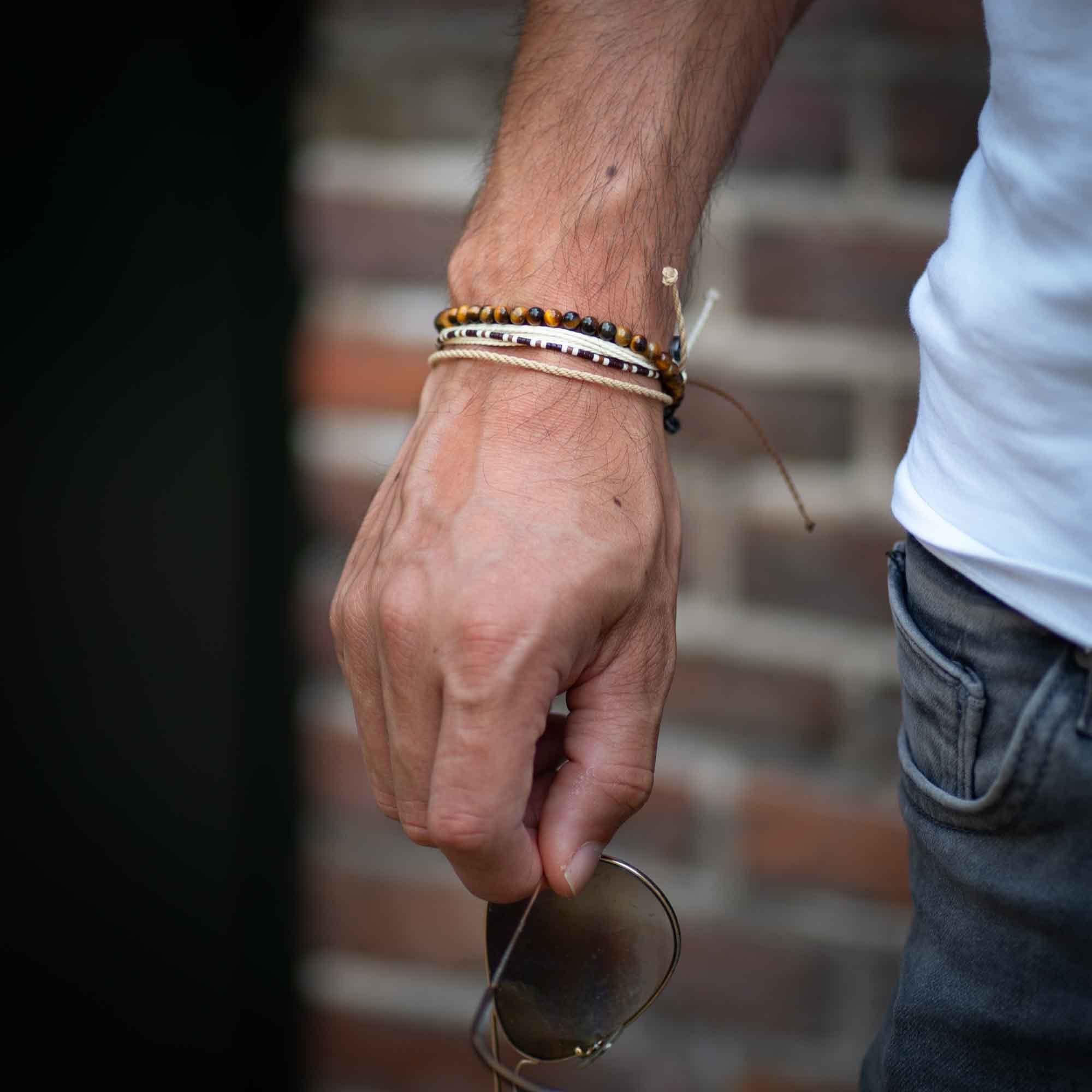 tiger eye bracelet pack on man's wrist who is holding Rayban sunglasses