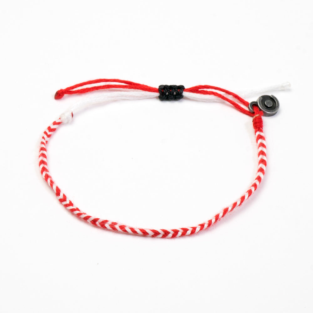 A bracelet with red and white woven pattern and a black gunmetal charm.
