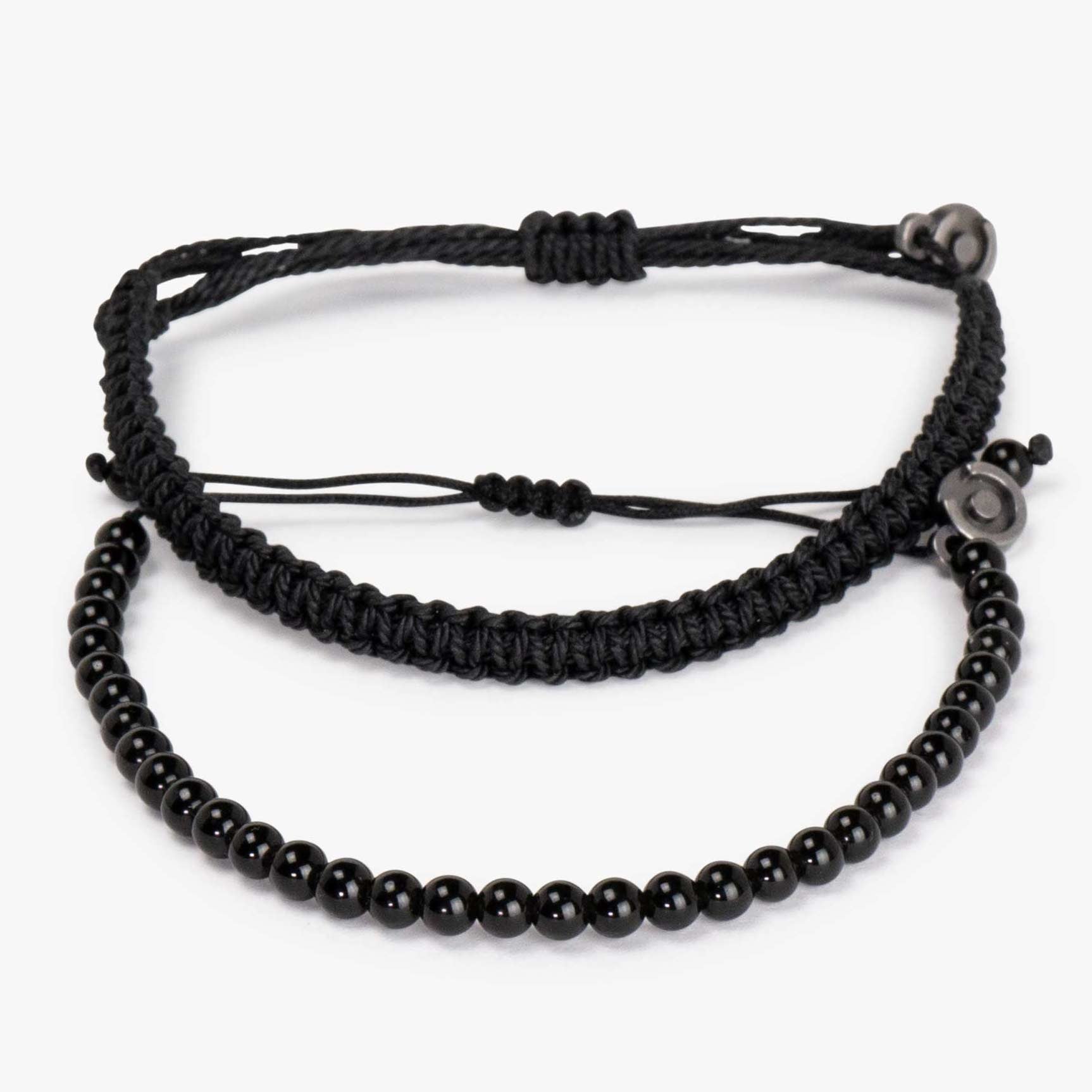Two black bracelets, one made of beaded black onyx gemstones and the other a solid black Cobra bracelet, with a gunmetal charm attached to the latter.