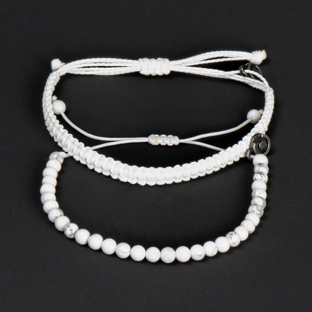 Two white bracelets made of howlite gemstones, displayed on a dark background. One bracelet has a charm and is wax-coated polyester, the other is just a howlite gemstone bracelet.