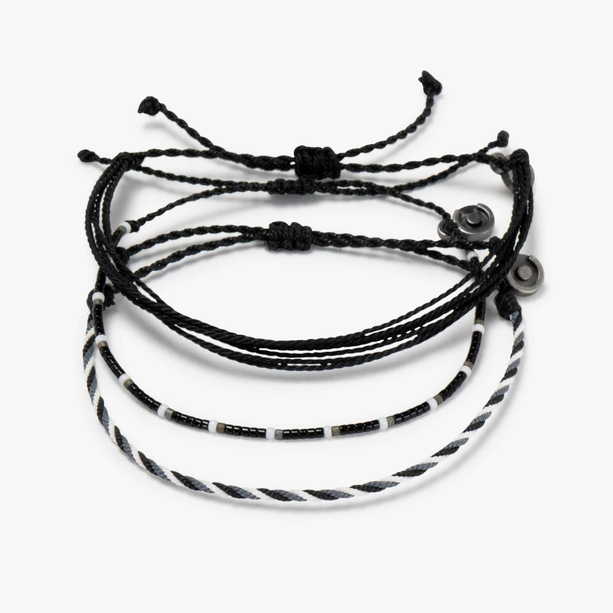 A set of three bracelets, two wax-coated polyester and one beaded, in black and white colors with a gunmetal charm, displayed against a white background.