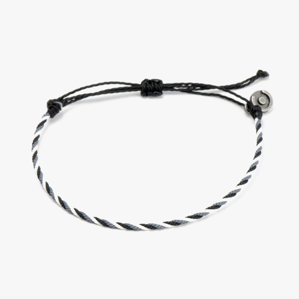 A black and white twisted bracelet with an adjustable loop and a gunmetal charm.