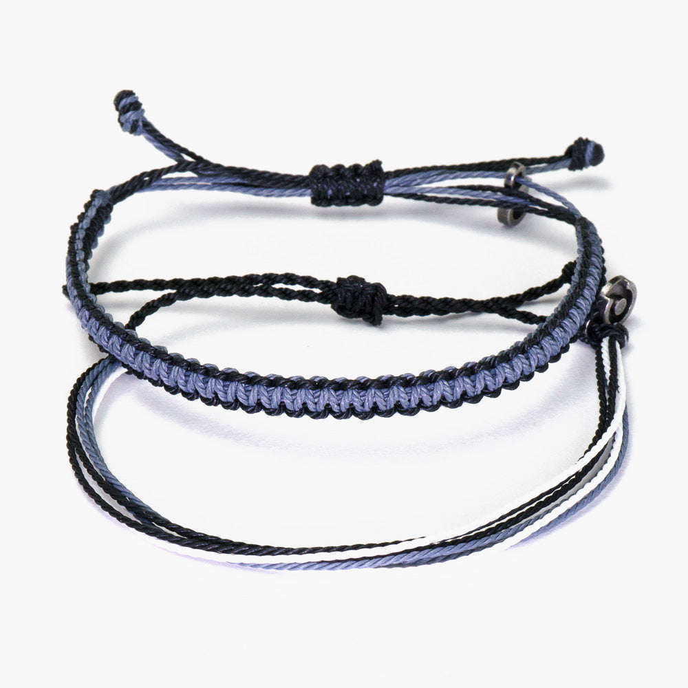 Two wax-coated polyester bracelets with a gunmetal power pose charm, one black and one blue, with adjustable knots.