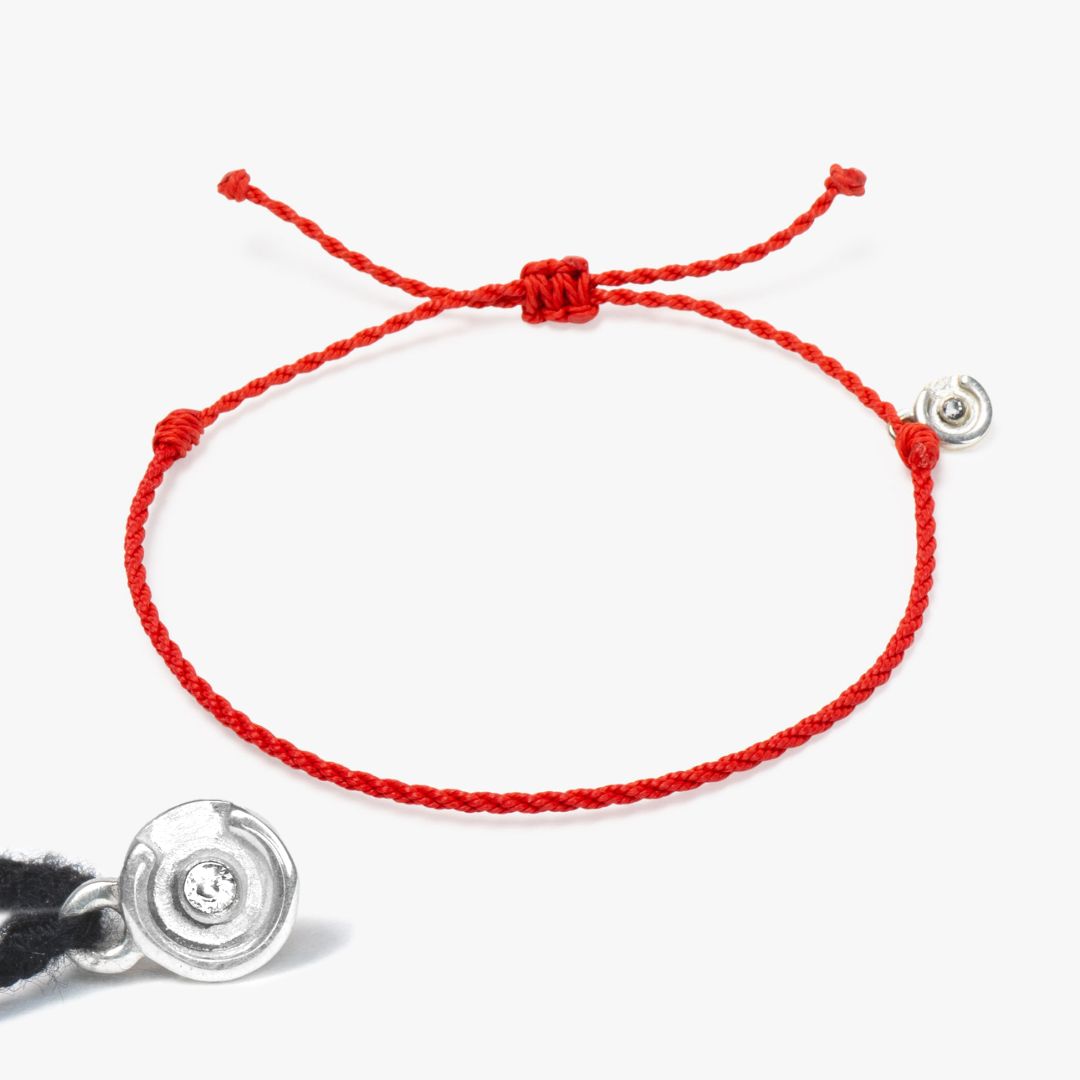 A red twisted bracelet with a silver and clear zircon stone charm, including a silver polish cloth.