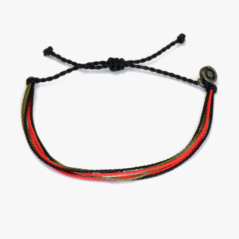 A bracelet with black, red, and green wax-coated polyester strands and a gunmetal charm, tied together.