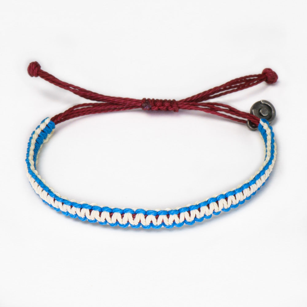 A two-tone blue and white woven bracelet with a gunmetal charm, featuring an adjustable red strap.