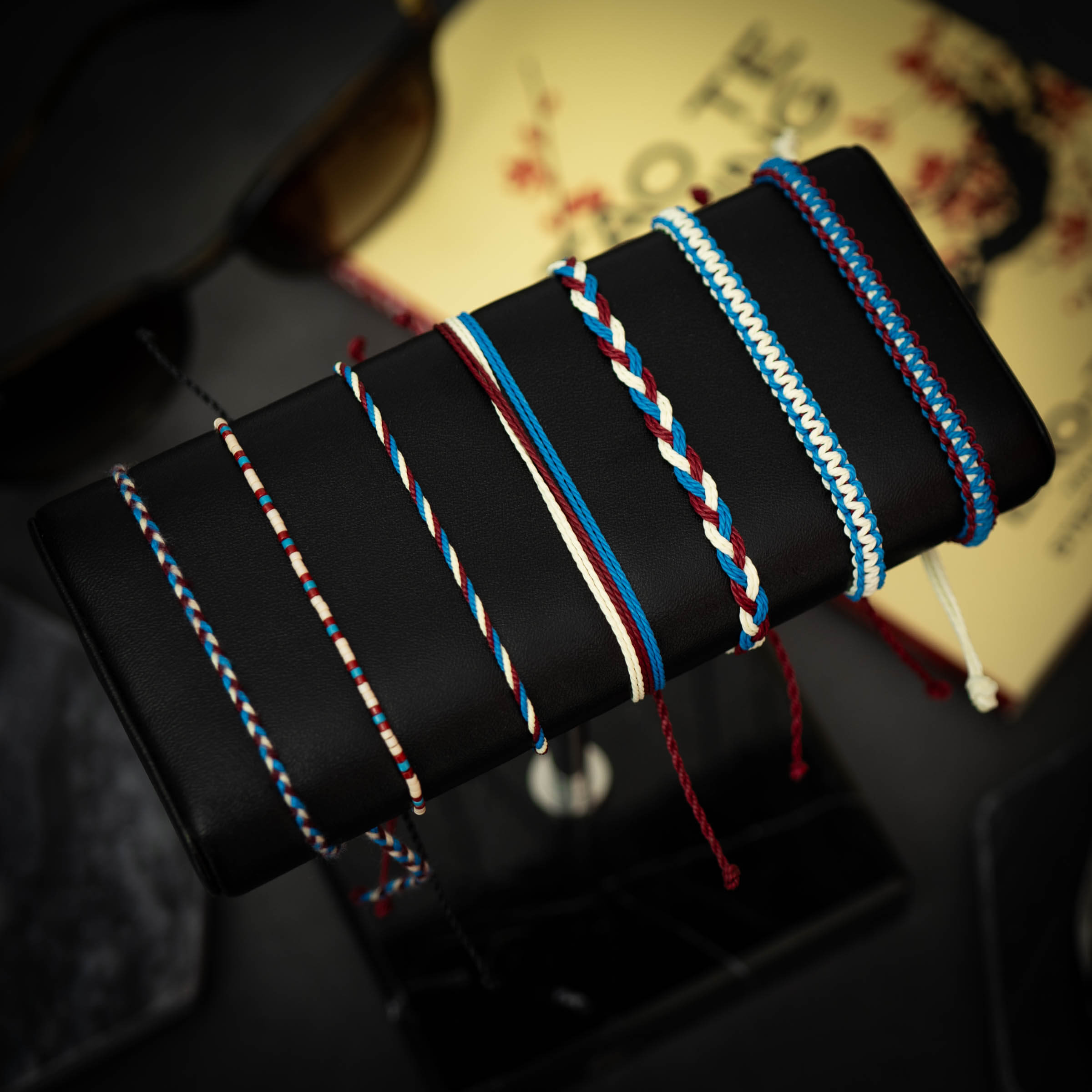 A collection of colorful woven bracelets displayed on a stand, featuring various designs and shades including blue, red, and white.