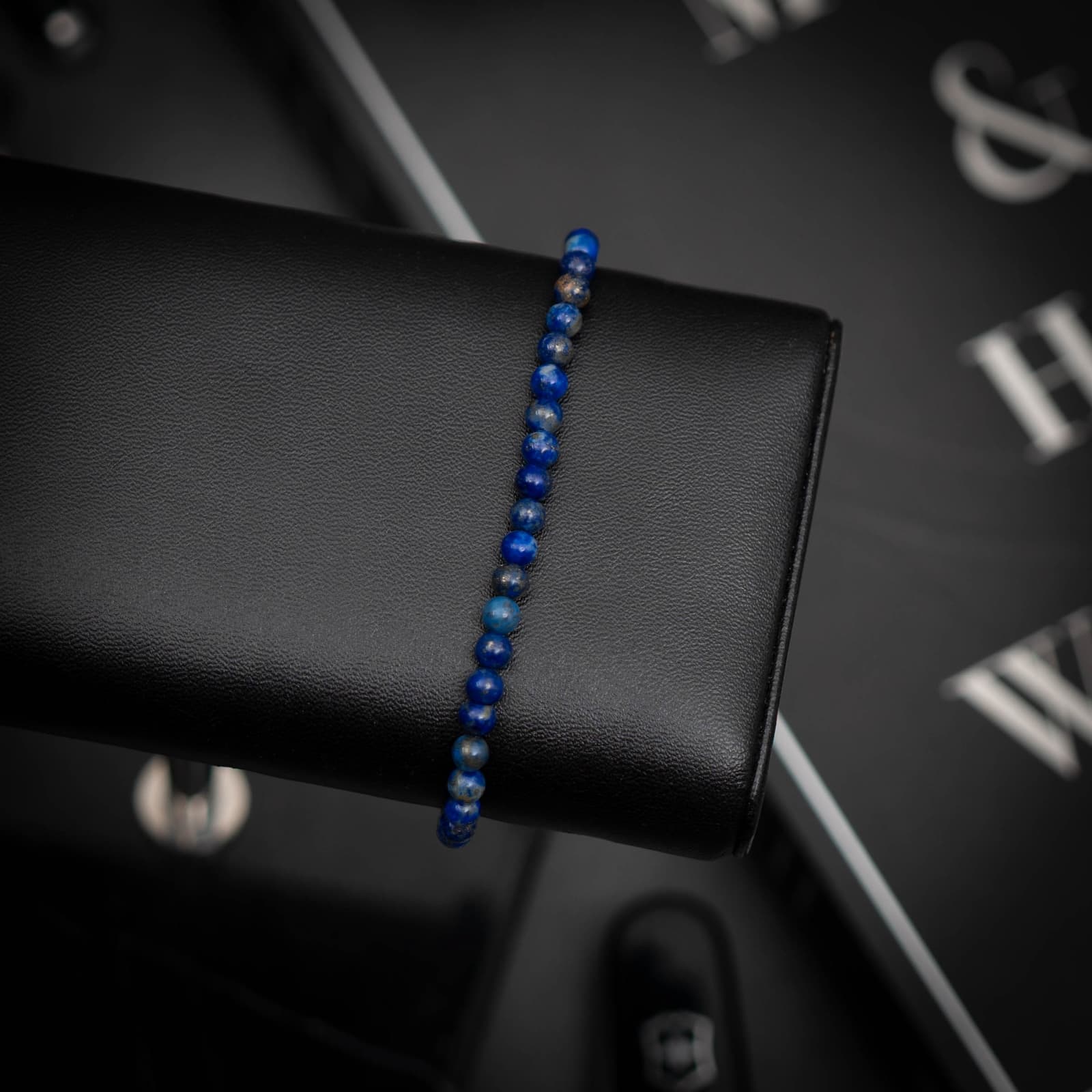 A Lapis Lazuli Gemstone Bracelet displayed on a black platform with a textured background.