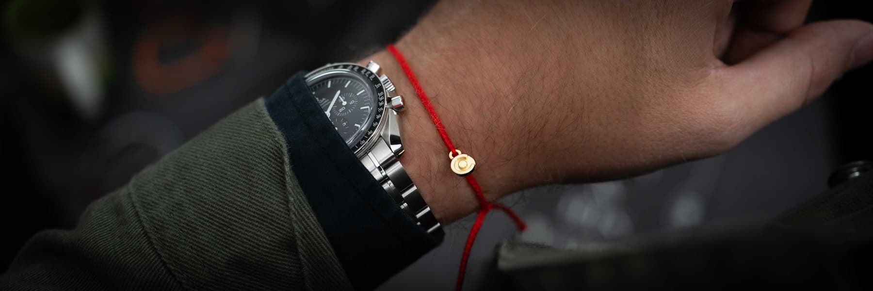 Hand wearing a black watch with a red string bracelet on a blurred background