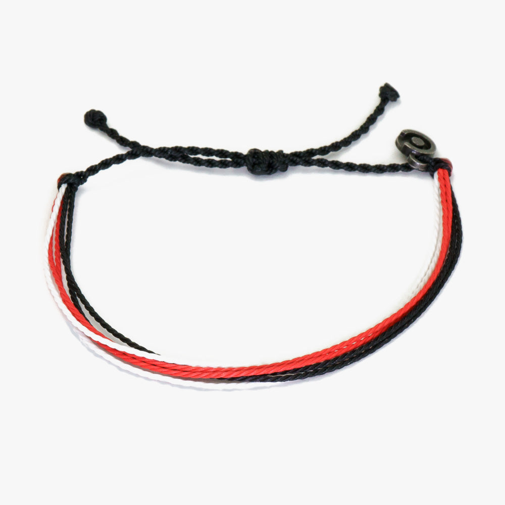 A Bali string bracelet with black, red, and white threads and a gunmetal power pose charm.