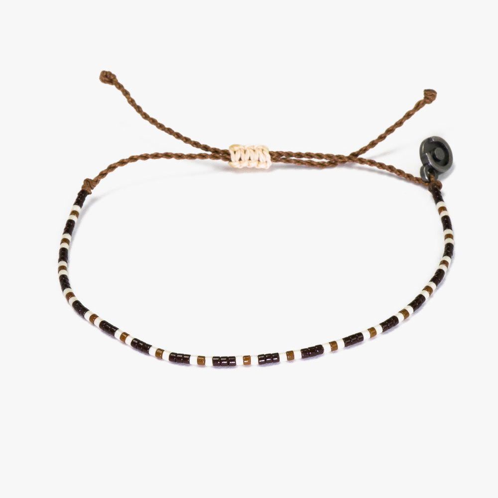 A brown and white beaded bracelet with a gunmetal charm, displayed on a white background.